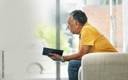Senior man, reading and thinking with book on sofa in home living room learning knowledge, information or ideas. Elderly, person and relax in retirement with novel, books or fiction with mockup space
