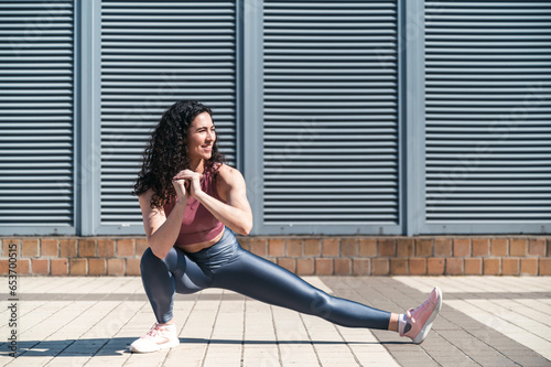 Young smiling fit woman doing stretching exercises for legs before training