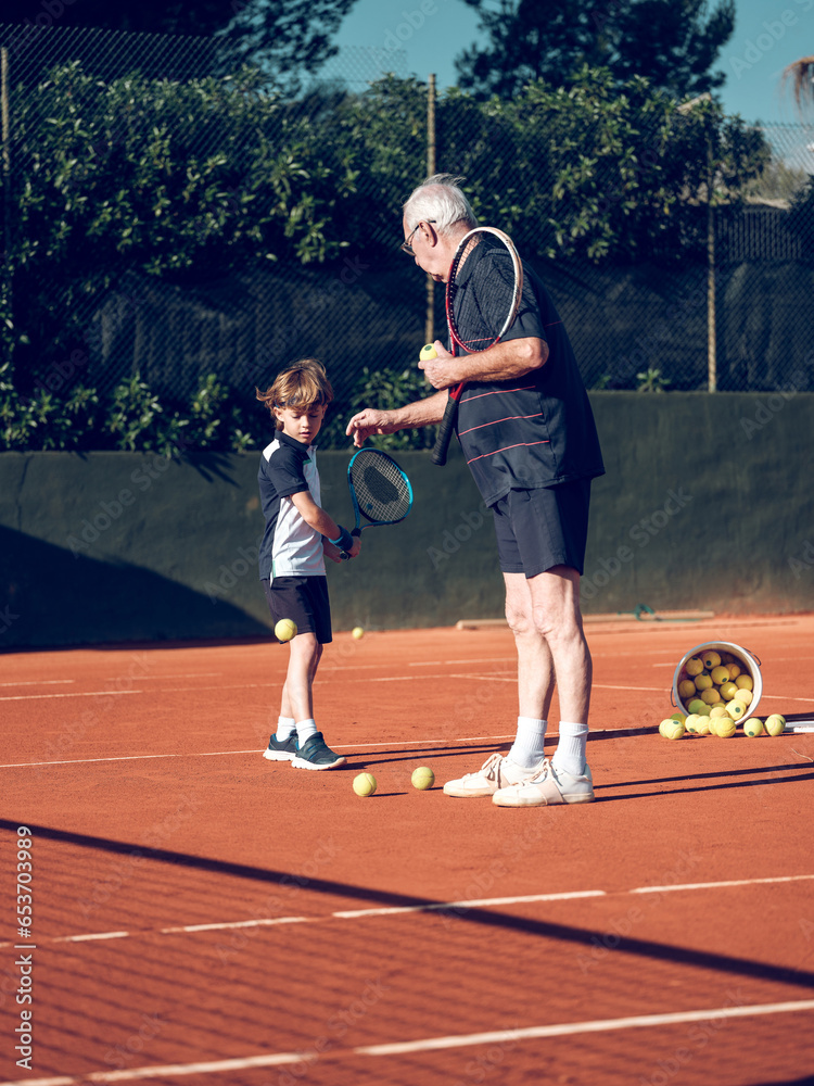Senior trainer explaining preteen boy with tennis racket techniq