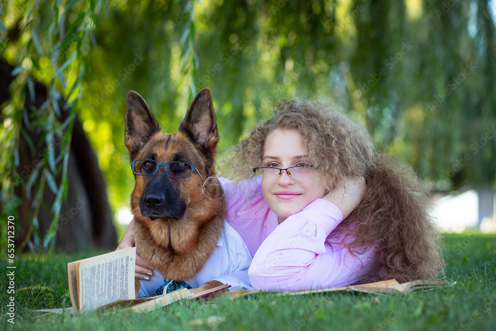  German Shepherd in white shirts and ties with a girl in glasses and a pink shirt, lying on the green lawn and reading books in the park