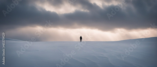 Wide-angle shot of a landscape of an empty snowy field and a silhouette of a man against the background of a gloomy winter sky with clouds. Cinematic composition. Impressive winter landscape.