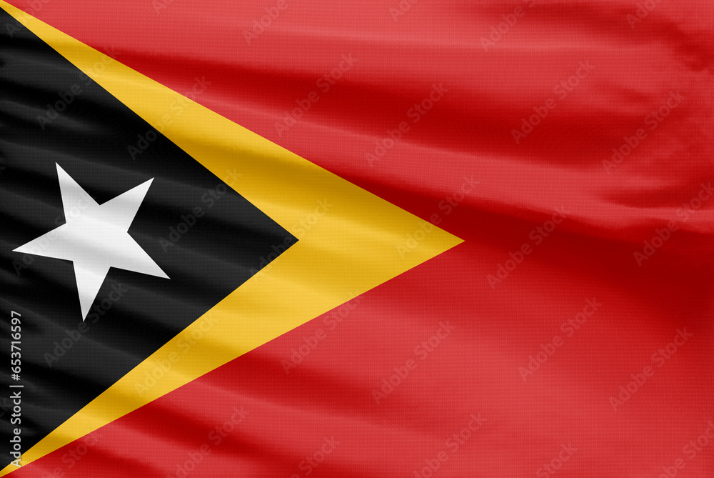 East Timor flag is depicted on a sport stitch cloth fabric with folds. East Timor flag is depicted on a sport stitch cloth fabric with folds.