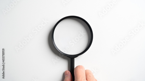 Hand holding magnifying glass isolated on white tabletop background.