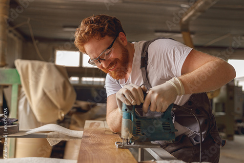 Cuadro en lienzo Professional carpenter cutting wood with an electric jigsaw machine in a carpent