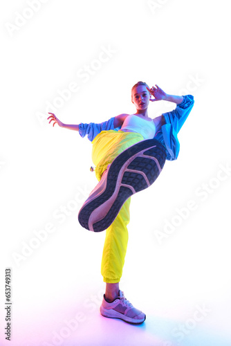 From below full body of attractive young woman training, dancing in trendy sport outfit and sneakers looking at camera in neon light.
