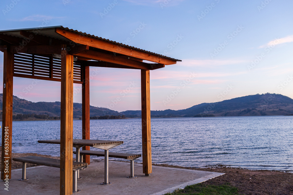 Lakeside picnic bench seating and shelter at dusk with lake and hills Lakeside picnic bench seating and shelter at dusk with lake and hills