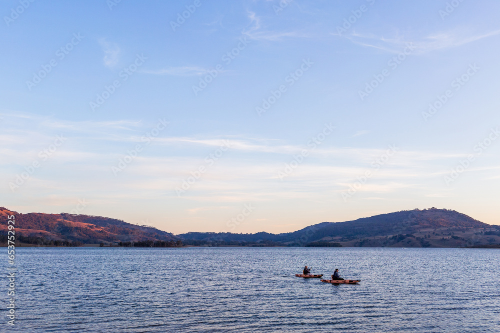 Kayaks on lake at dusk paddling on rippling water Kayaks on lake at dusk paddling on rippling water