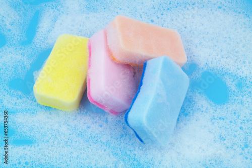 Different sponges with soap foam on blue background.	