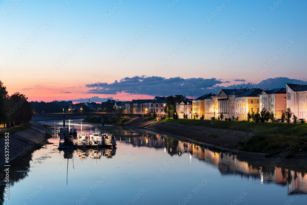 Vologda River with a pier and tourist boats and Prechistenskaya embankment at dawn. Vologda, Russia