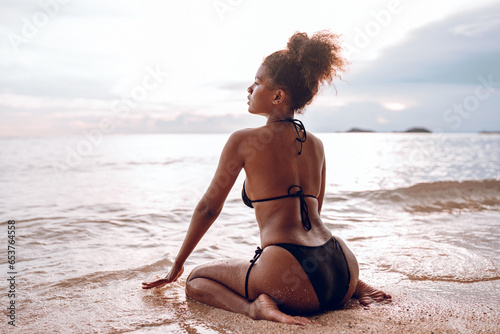 Fototapeta Naklejka Na Ścianę i Meble -  Beautiful African american woman in pink bikini on tropical beach. Portrait of dark skinned woman smiling at sea. Brunette tanned girl in swimwear enjoying and walking on beach.