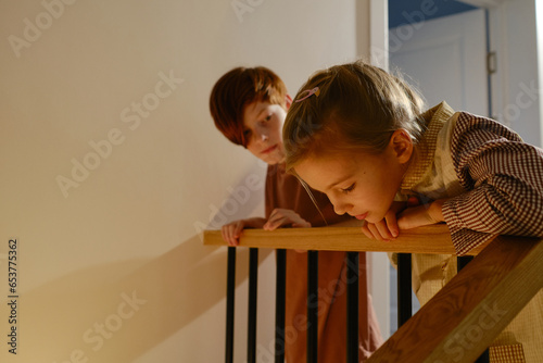Horizontal shot of little boy and girl wearing pyjamas standing upstairs looking at something beneath then at each other photo