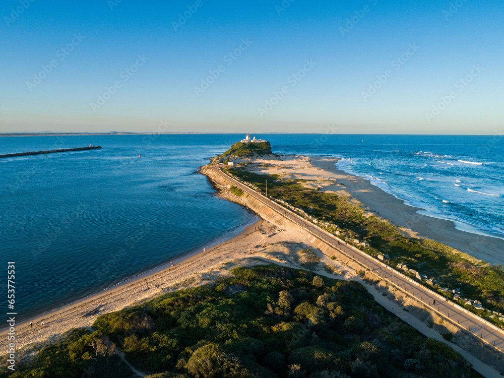 Nobbys Lighthouse on headland surrounded by blue water