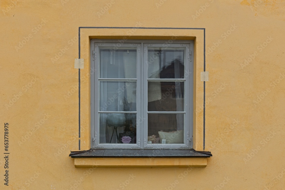 Window with frame painted grey on a yellow stone wall.