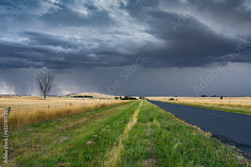 Low angled view of dark storm clouds and rain advancing over a road through a rural setting photo