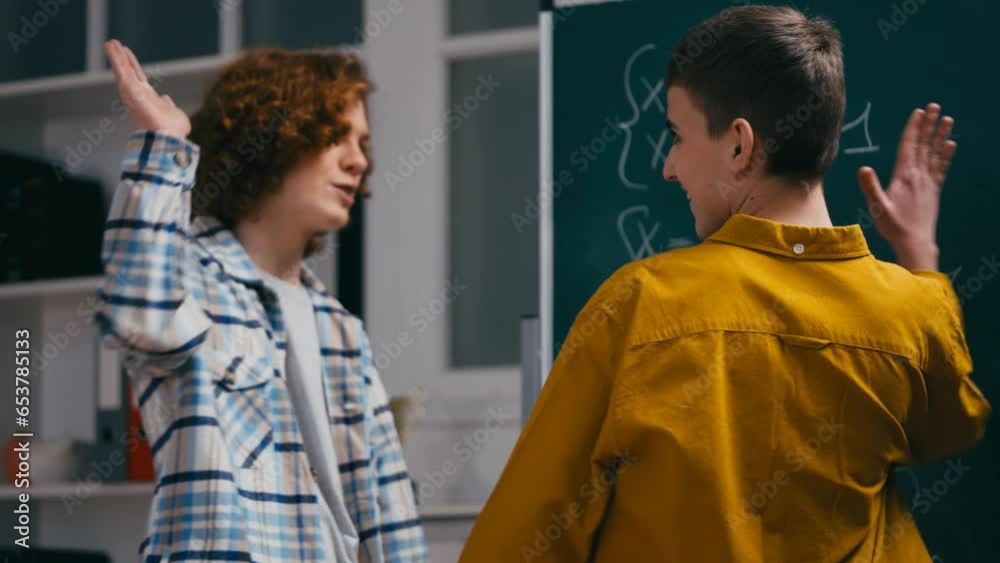 Teen boy helping classmate with math equation near chalkboard, giving high five Teen boy helping classmate with math equation near chalkboard, giving high five