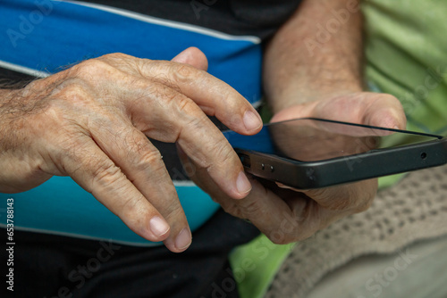 Detalhe das mãos de um homem idoso que está usando um telefone celular. photo