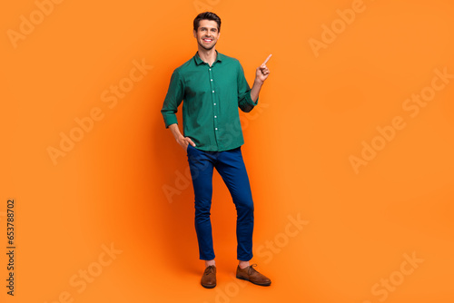 Full body photo of young man wear green shirt pants classics shoes direct finger brand store clothes isolated on orange color background © deagreez
