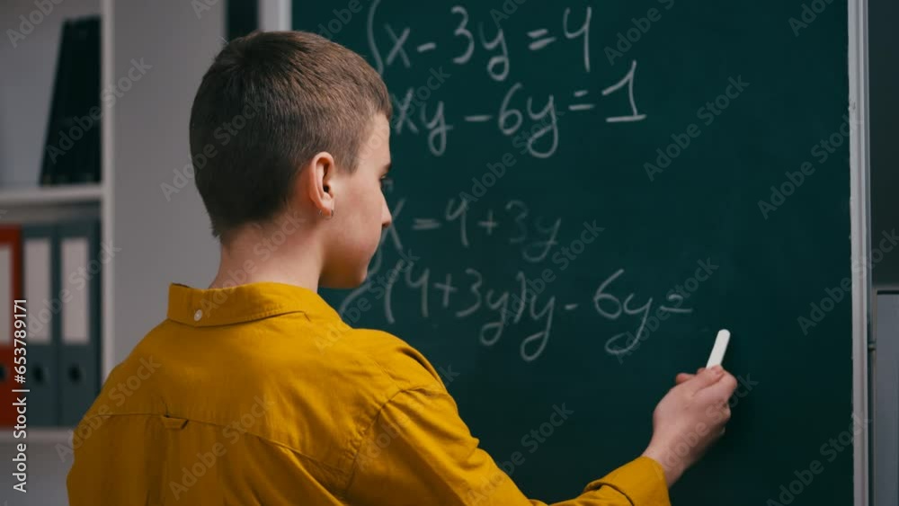 Teenage boy trying to solve math equation near chalkboard, scratching his head Teenage boy trying to solve math equation near chalkboard, scratching his head