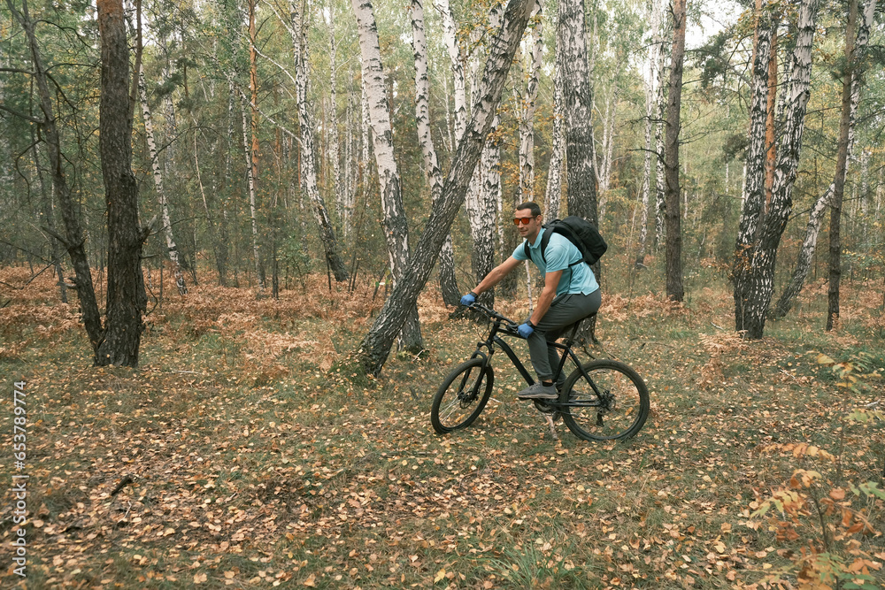 man with a backpack and glasses rides a mountain bike in autumn through the forest.An active lifestyle.Cycling