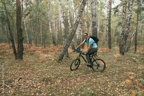 man with a backpack and glasses rides a mountain bike in autumn through the forest.An active lifestyle.Cycling
