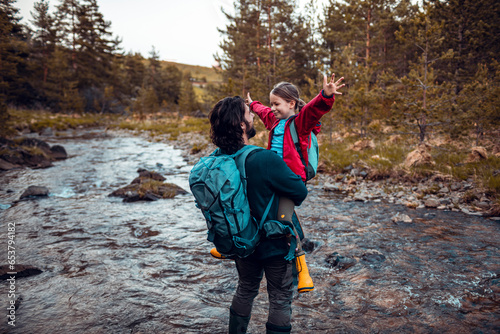 Young father and daughter crossing a creek while out hiking in the forest and mountains