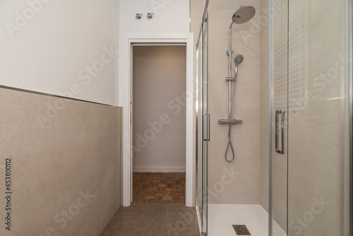 Small bathroom in an apartment with shower cabin with glass partitions and walls of marble tiles and white paint