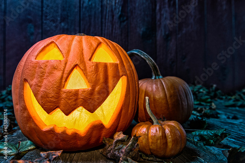 A close-up of a glowing smiling Jack O' Lantern basking in the blue moon light while sitting on an old weathered wooden deck.  photo