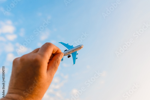 Toy airplane in a man's hand on a background of the sky with clouds.Man holding airplane in hand and flying over the cloudy sunset blue sky background.Travel motivation concept.