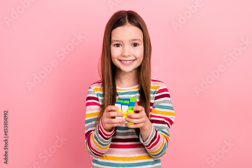 Photo of optimistic small little funky kid girl playing rubik cube toy logic puzzle solving strategy isolated on pink color background