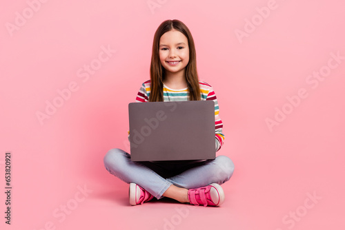 Full size body photo of little gamer cute girl have fun playing her cool laptop advertising device isolated on pink color background © deagreez