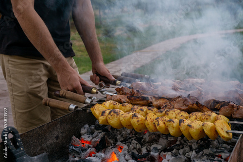 Male hands cooking meat on skewers on barbecue grill outdoors