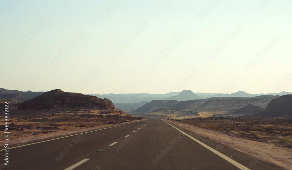 Empty asphalt road in the desert at sunset. Sand mountains on the roadside and horizon.