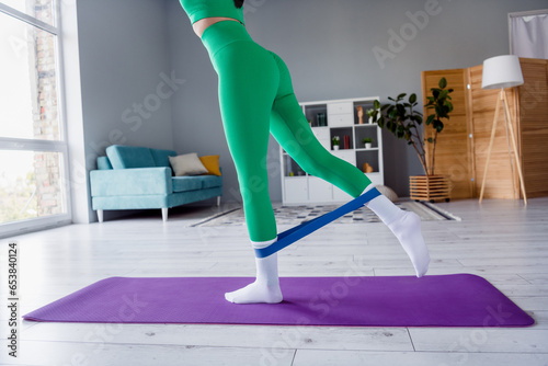 Photo of sexy slim young girl dressed sportive suit standing yoga mat doing legs elastic rubber exercise indoors house home photo