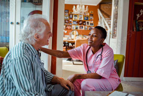 Young African American female caregiver consulting her senior patient at home photo