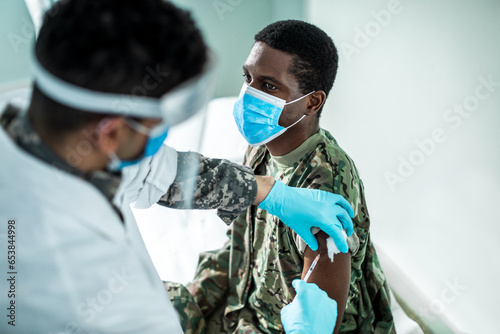 Young army man getting vaccinated by a health worker at the clinic photo