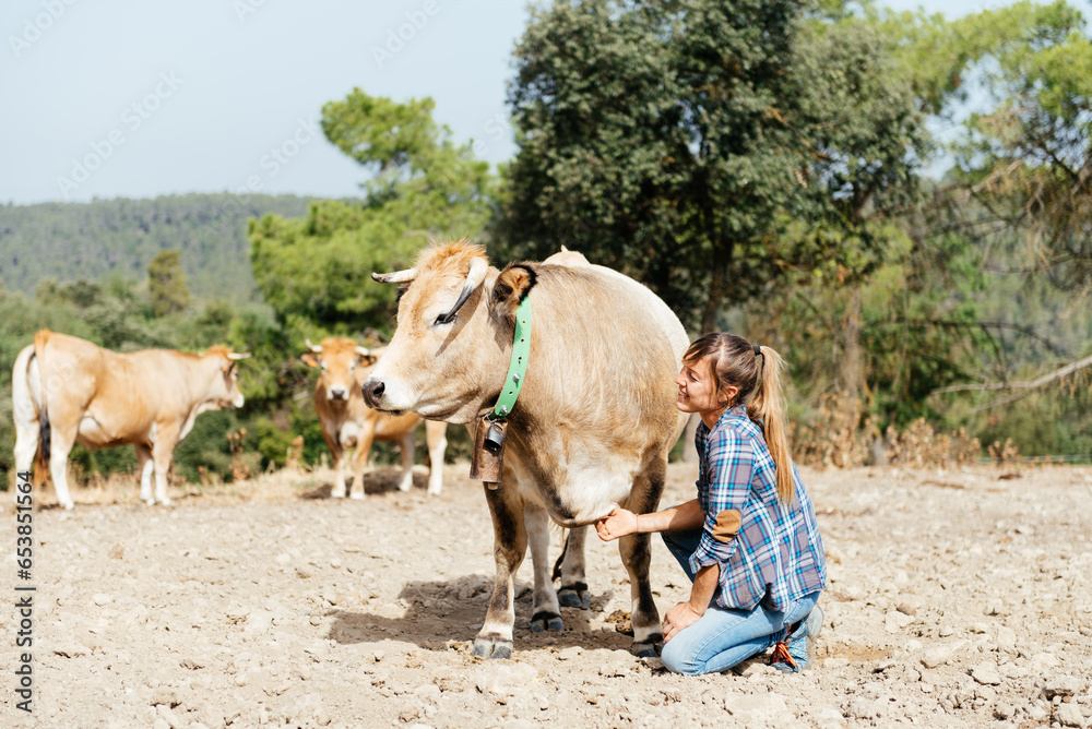Young woman kneeling and stroking cow in countryside