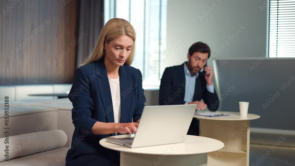 Caucasian male and female employees dressed in formal business wear using modern gadgets for work at bright office. Attractive woman typing on laptop while handsome man talking on smartphone. Caucasian male and female employees dressed in formal business wear using modern gadgets for work at bright office. Attractive woman typing on laptop while handsome man talking on smartphone.