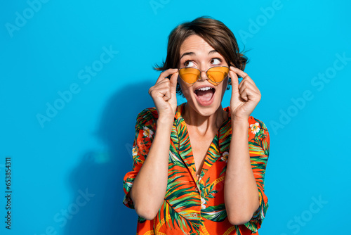 Portrait of cheerful impressed lady arms touch sunglass open mouth look empty space isolated on blue color background