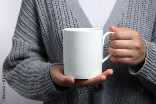Woman holding white mug on light gray background, closeup. Mockup for design