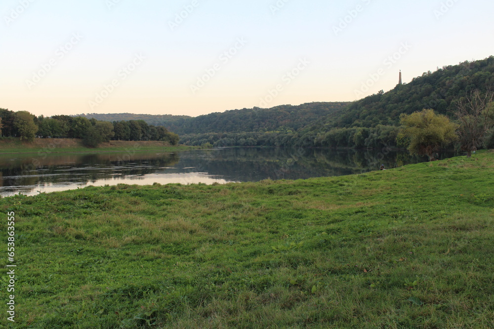 A grassy field with a river and trees in the background