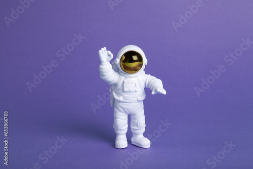 an astronaut figurine in a spacesuit exploring a plain purple background