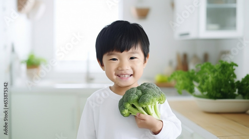 Little beautiful asian boy posing with broccoli in the kitchen. Healthy vegan baby foods concept.