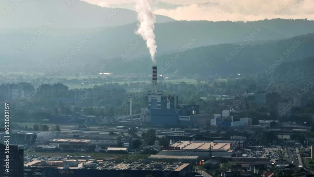 Aerial view of an industrial area in Slovenia, with a prominent chimney emitting smoke. Aerial view of an industrial area in Slovenia, with a prominent chimney emitting smoke.
