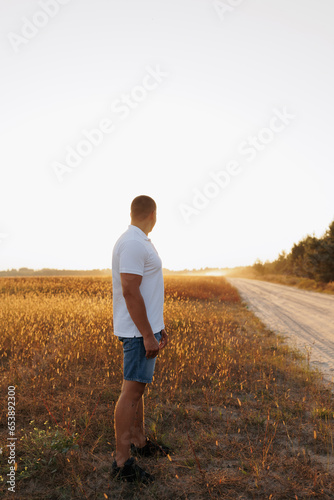 A handsome strong guy in a white t-shirt stands in a field at sunset