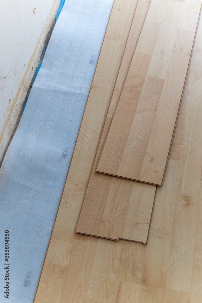 A vertical portrait of a stacked pile of wood imitation laminate floorboards lying on some sound isolation ready to be installed to create a wooden floor in a house on a screed floor.