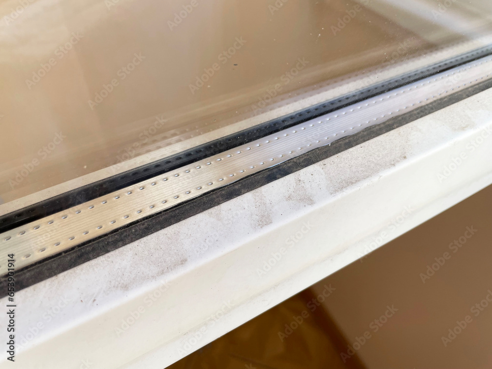 A fragment of a dirty window frame, glass and the sill of a metal-plastic window with a black thin rubber band around the perimeter, close-up, side view. The window is covered with dirt and dust. A fragment of a dirty window frame, glass and the sill of a metal-plastic window with a black thin rubber band around the perimeter, close-up, side view. The window is covered with dirt and dust.
