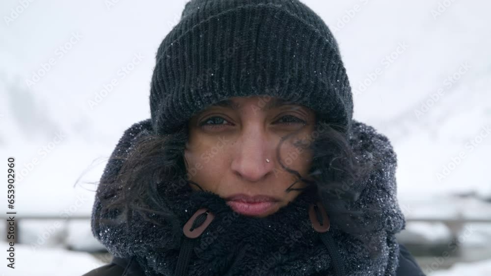 Medium close-up of Indian middle-aged woman with dark skin, nose piercing in black knitted hat looking into camera, smiling, outdoors during blizzard. High quality 4k footage Medium close-up of Indian middle-aged woman with dark skin, nose piercing in black knitted hat looking into camera, smiling, outdoors during blizzard. High quality 4k footage