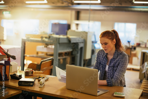 Young woman using a laptop while working in a printing press office