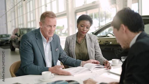 Middle aged interracial couple closing the deal with a salesmen on their new car at the dealership