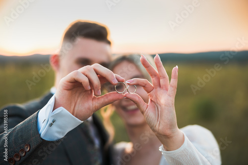 bride and groom are together happy and full of love holding wedding rings, wedding photoshoot in the middle of nature, bride in a white dress, groom in a stylish suit, wedding day, love